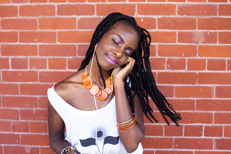 Black woman listening to earbuds near brick wall